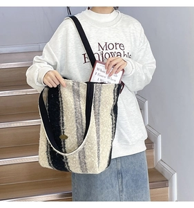 Detail of plush striped tote bag featuring wide black straps and metallic logo plate