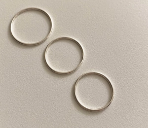 Detailed view of three minimalist 925 sterling silver slim rings on a white textured base
