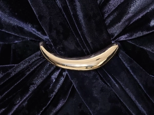 Detailed macro view of an elegant gold curved metal buckle on dark velvet fabric