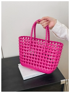 Pink hollow woven jelly basket bag held by a hand over a decorative art book