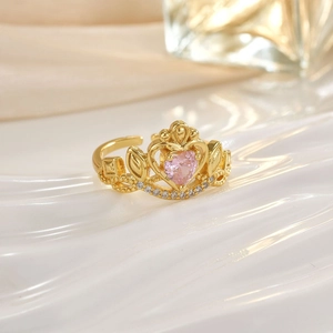 Macro detail of a golden crown ring with a pink heart gemstone on soft white silk fabric