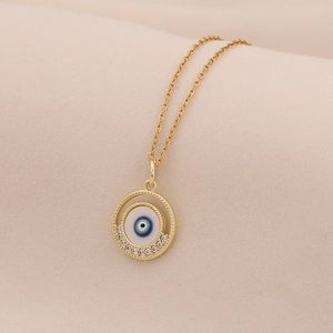 Detail of gold evil eye necklace with crystals on beige fabric backdrop