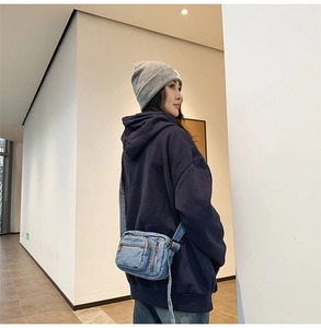 Detail of light blue washed denim crossbody bag with multiple zippers on a casual outfit