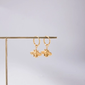 Detailed view of 18K gold-plated stainless steel bee earrings on a metal display stand