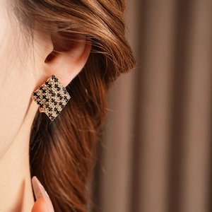 Détail d'une boucle d'oreille carrée dorée avec motif damier en cristaux noirs et blancs