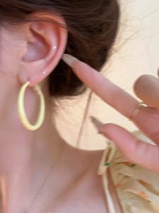 Close-up of a model wearing large matte yellow hoop earrings in a summer style