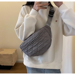 Detail of grey quilted crossbody bag with adjustable wide strap and buckle on model