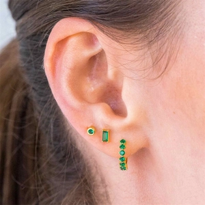 Detail view of gold-plated stud set featuring emerald green gemstones on model ear