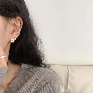 Close-up of minimalist silver oval earrings and ear cuffs styled on a model's ear