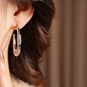 Close-up of twisted silver-tone C-shape earrings with zircon stones worn by a model