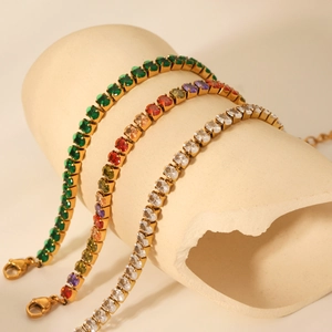 Macro detail of three gold tennis bracelets with emerald, rainbow, and clear stones