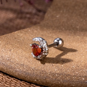 Macro detail of gothic bat heart earring with red zircon on a natural stone background