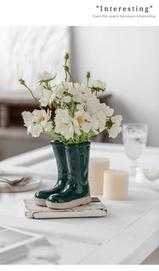 Detail of dark green ceramic rain boot vases with white daisies in a home setting