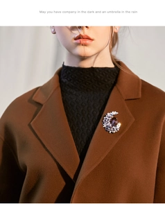 Detail of a crescent moon brooch with large gemstone on a brown wool coat