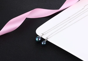 Detailed view of dark green pearl pendants on delicate silver chains over white tray