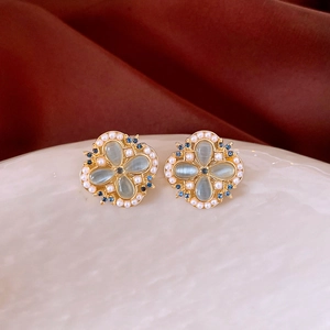 Detail view of flower-shaped clover earrings with grey-blue cat eye stone and white pearl