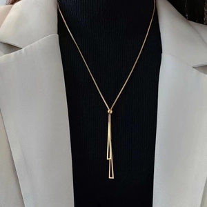 Minimalist long gold necklace with geometric double triangle tassel on a model dress