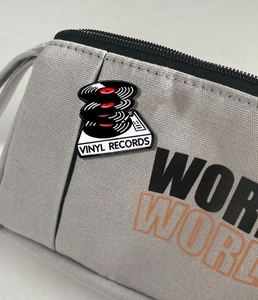 Detail of a vintage vinyl record player enamel pin on a gray canvas textured bag
