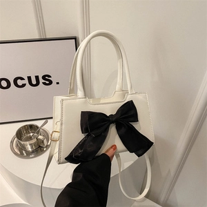 Modern white handbag with black bow decoration and crossbody strap held by a person