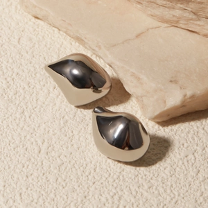 Macro view of polished silver water drop earrings on a natural textured stone base