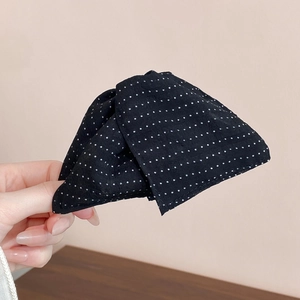 Close-up of black and white polka dot fabric hair clip with a minimalist bow design