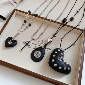 Vintage cross and black heart pendant necklaces with leather details on wooden tray