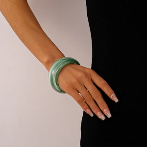 Detail of a wide green acrylic cuff bracelet with marbled texture on a woman's wrist