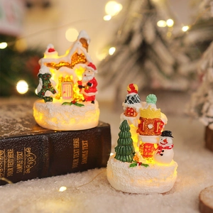 Close-up of glowing resin gingerbread house with Santa and snowman on fake snow