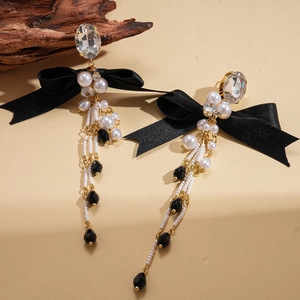 Detail of long bow earrings with black ribbons and pearls on a vintage wood background