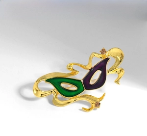 Macro shot of gold mask brooch featuring green and purple enamel with amber rhinestones