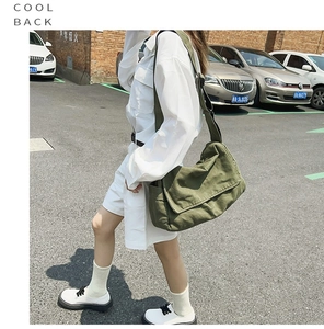 Street style shot of army green canvas tote bag worn as a crossbody bag by a model