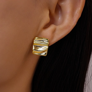 Close-up of golden rectangular earrings with wavy texture worn by a model