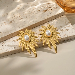 Detailed view of gold palm leaf earrings with an elegant oval pearl on a stone base