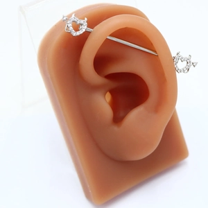 Vista macro di un piercing industriale con cuore e freccia su un modello di orecchio in silicone