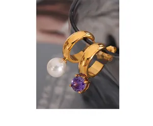Detail of asymmetric gold C-shaped hoop earrings with a white pearl and purple zircon gem