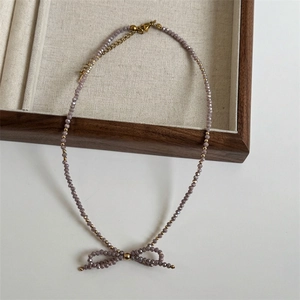 Macro detail of hand-woven purple crystal beaded necklace with bow pendant on linen tray