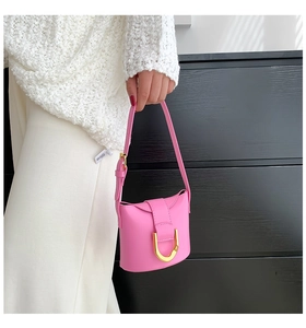 Detail of a bright pink leather mini handbag featuring a distinctive gold D-ring buckle