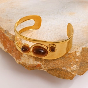 Close-up of golden hollow oval bracelet featuring amber-colored stones on a natural rock base