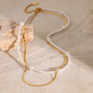 Double-layered golden snake chain and white pearl necklace on marble surface