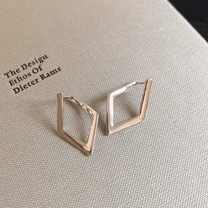 Macro shot of silver geometric diamond-shaped huggie earrings on a textured book surface