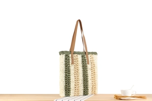 Straw tote bag detail with green stripes, leather handles, and summer vacation vibe