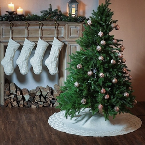 Detail of cream cable knit Christmas tree skirt and matching stockings in festive setting