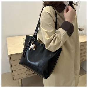 Close-up of black leather tote bag with baseball pendant accessory shown on model's shoulder