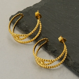 Macro detail of gold geometric hoop earrings with beaded texture on a stone surface