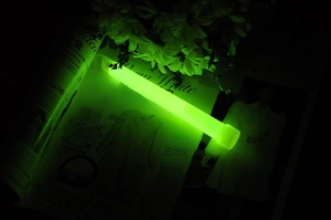 6-inch green glow stick with hook emitting bright light on an open magazine in the dark