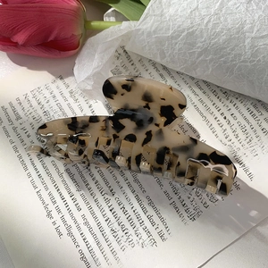 Detail of large leopard print acetate shark hair claw clip placed on a book with tulips