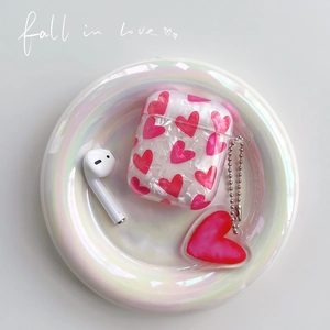 Pearlescent heart pattern AirPods case with red heart charm on iridescent dish