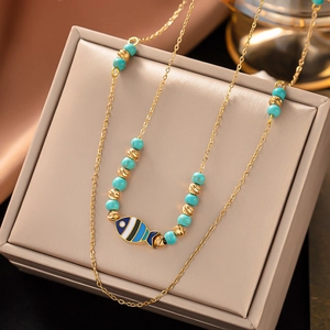 Detail of bohemian gold chain necklace with turquoise beads and fish pendant on a jewelry box