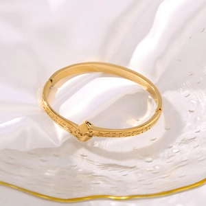 Golden stainless steel cuff bracelet with rock texture on white silk satin background