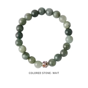 Close-up of green beaded bracelet with a silver-hued hollow charm and colorful gemstones